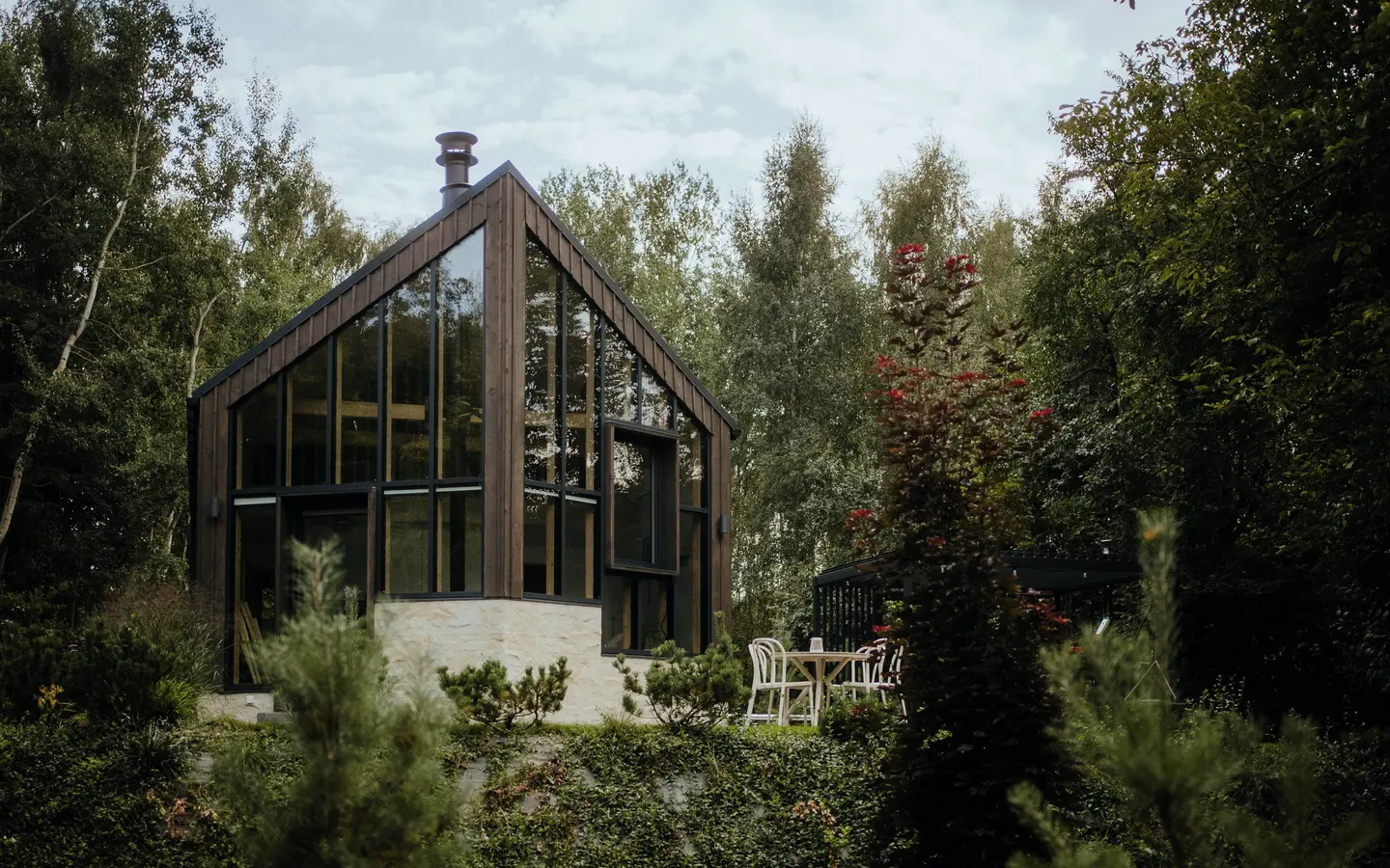 A wooden cabin at dusk with a string of lights and warmly lit windows among greenery