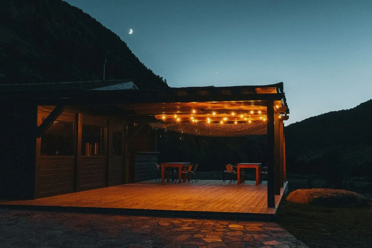 Wooden deck with a string of lights at dusk, a mountain slope in the background