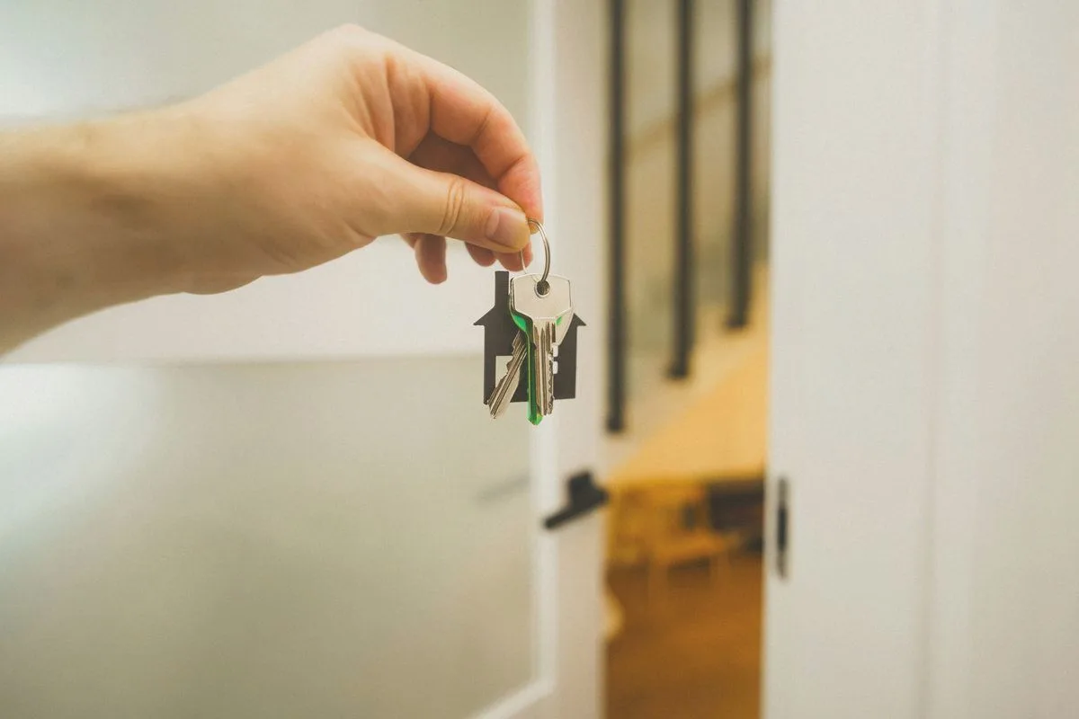 A hand with keys on a house-shaped fob by an open door